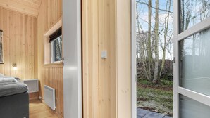 Un intérieur en bois avec un lit, un radiateur et une fenêtre donnant sur une forêt.