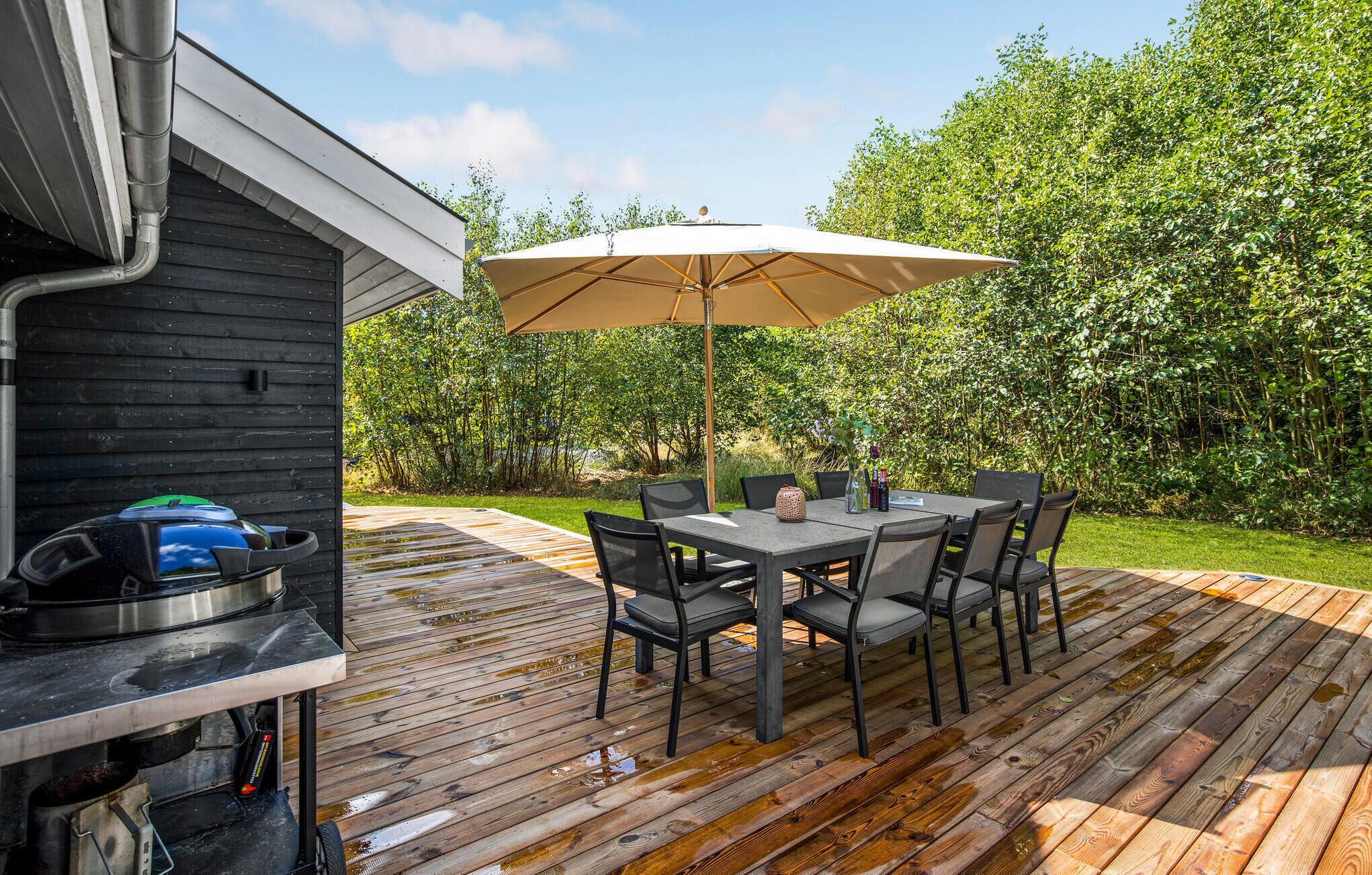 A wooden deck with a table and chairs, an umbrella, and a grill.
