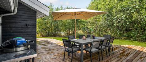 A wooden deck with a table and chairs, an umbrella, and a grill.