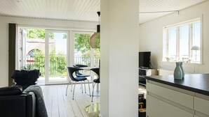 A modern kitchen with a large window, a dining area with a table and chairs, and a view of greenery outside. - 2 bedroom cozy home in Svaneke (Svaneke)