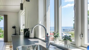 A kitchen with a stainless steel sink, a window with a view of the sea, and a potted plant on the windowsill. - 2 bedroom cozy home in Svaneke (Svaneke)
