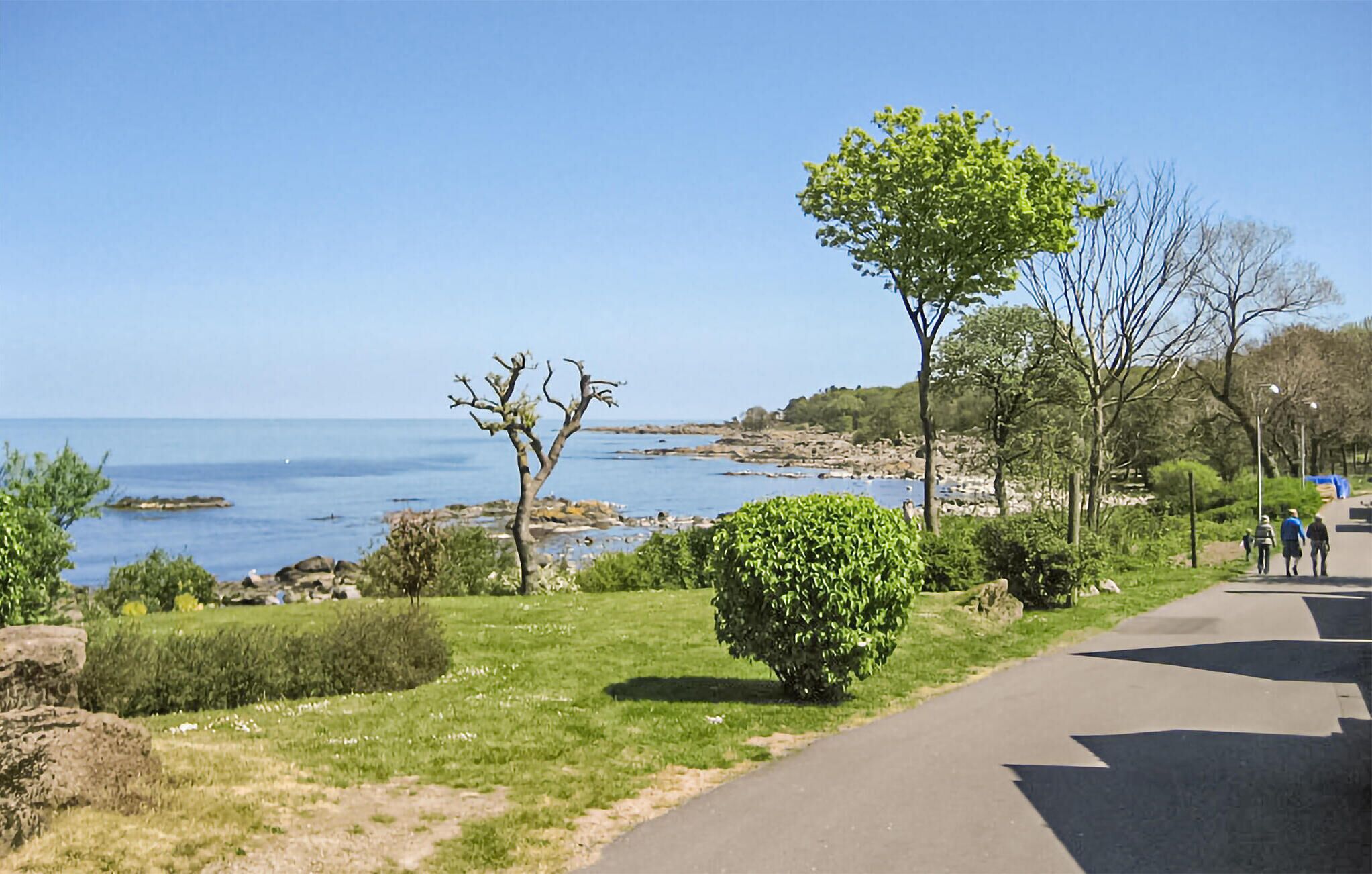 A coastal walkway with a clear view of the sea, surrounded by greenery and trees.
