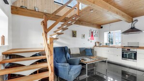 A modern kitchen with a wooden staircase, a dining area with a blue sofa, and a kitchen island. - Beach front apartment in Nexø with WiFi (Nexø)