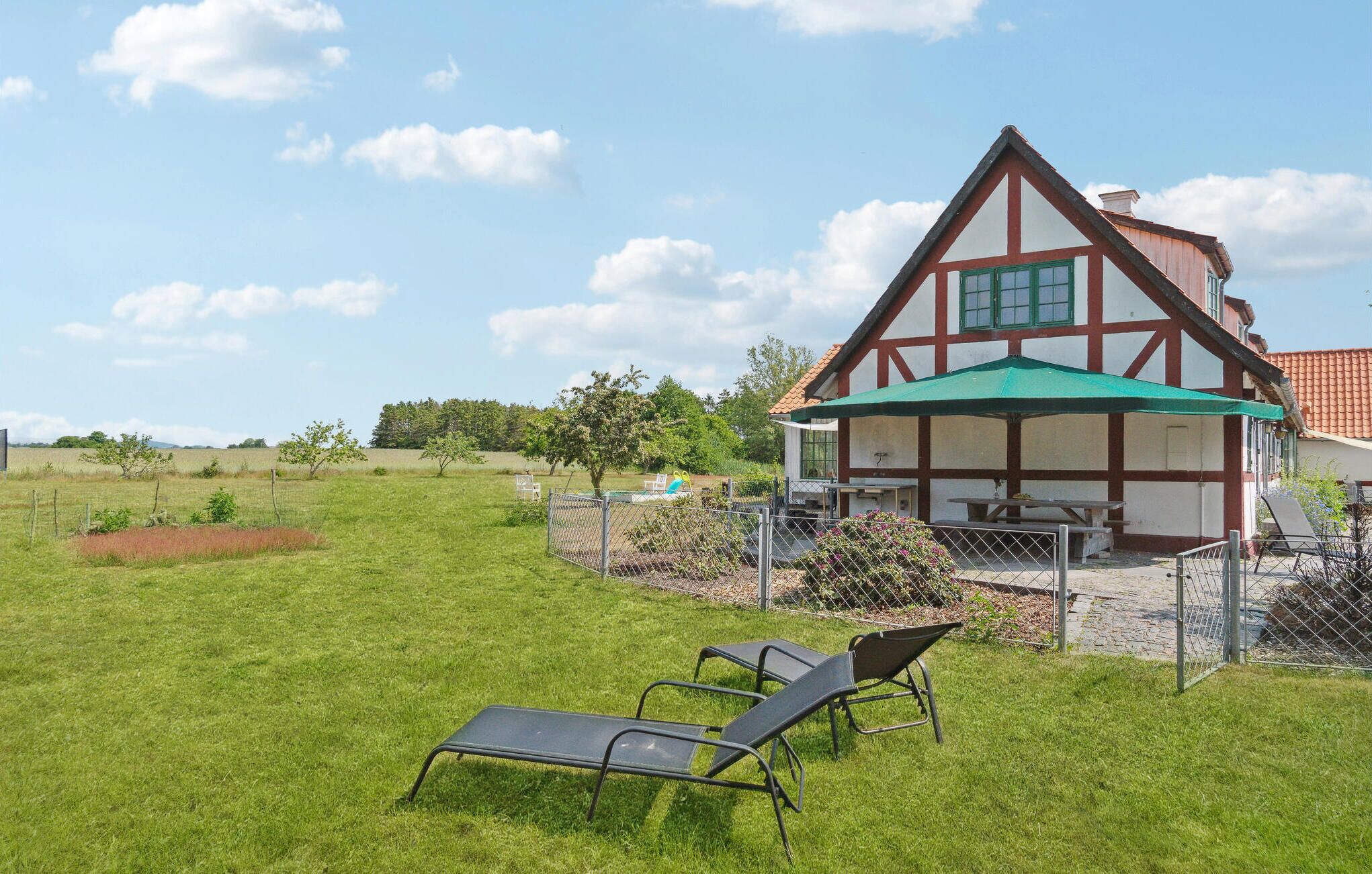 Ein traditionelles Fachwerkhäuschen mit grünem Sonnenschirm, einem umzäunten Garten und zwei Liegestühlen.