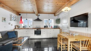 A modern kitchen with white cabinets, a wooden dining table, and a TV mounted on the wall. - Beach front apartment in Nexø with WiFi (Nexø)