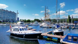 A marina with various boats docked, a large building in the background, and a clear blue sky. - Res. Vent de Sable ref.: 115 (Oostende)