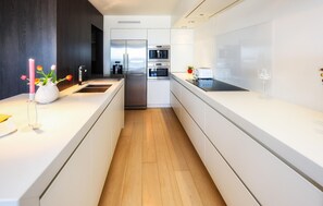 A modern kitchen with white cabinetry, a stainless steel refrigerator, a built-in oven, and a coffee machine.