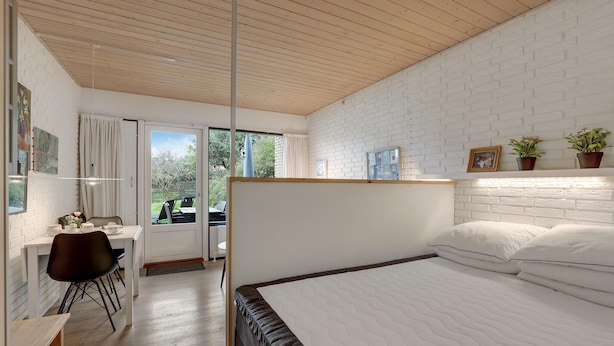 A modern bedroom with a large bed, a desk with a chair, and a view of the outdoors through a glass door. - Amazing apartment in Allinge (Allinge)