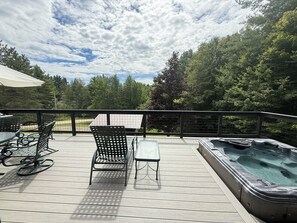 A deck with outdoor furniture, a hot tub, and a view of a forested area.