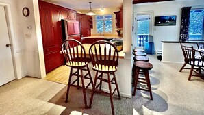 A kitchen with wooden cabinets, a dining area with chairs, and a view of the outdoors through a window. - MINUTES TO STRATTON AND BROMLEY! (bondville)