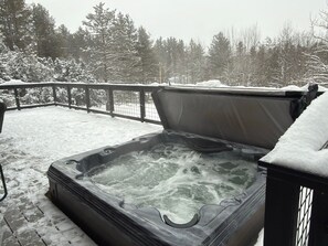 A hot tub on a snow-covered deck with a view of trees.