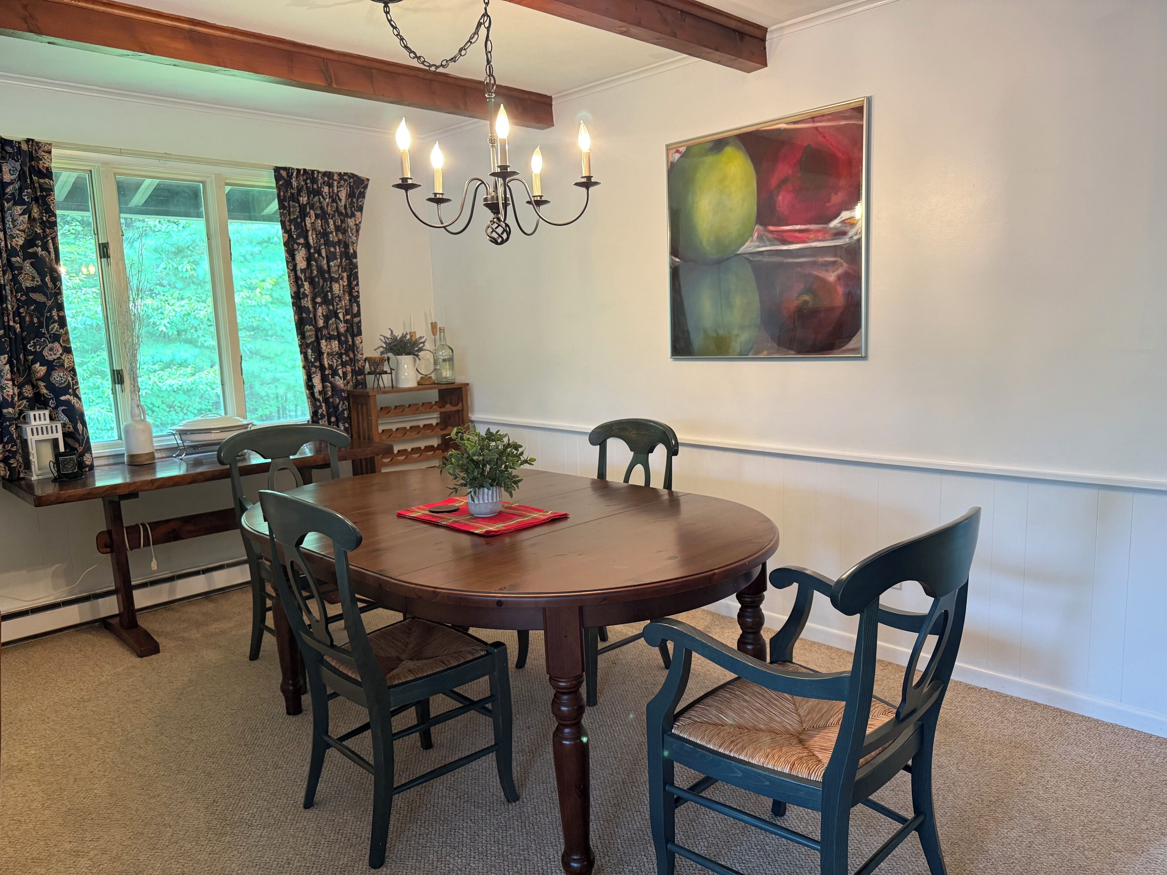 A dining room with a wooden table and chairs, a chandelier, and a window with curtains.