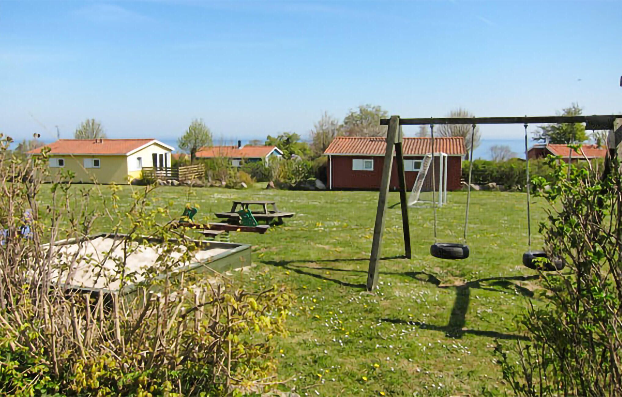 Ett grönområde utomhus med en gunga, ett picknickbord och ett förråd.