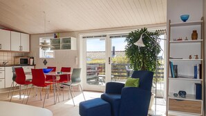 Una cucina moderna con mobili bianchi, un'area pranzo con sedie rosse, una poltrona blu e una libreria.