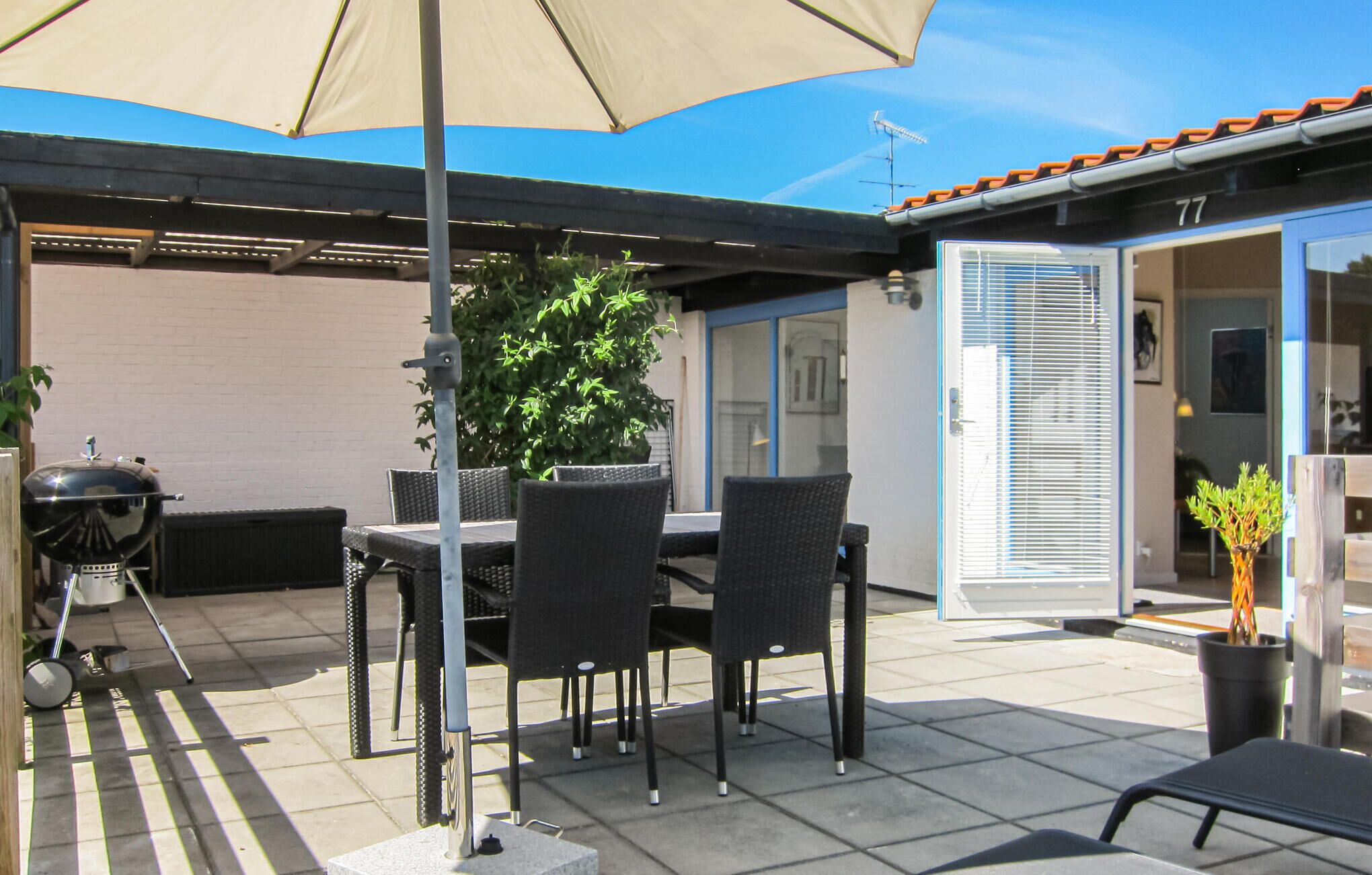 Une terrasse extérieure avec une table et des chaises, un barbecue et une plante en pot.