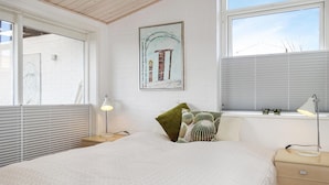 Una camera da letto con un letto, due lampade da comodino, una finestra con persiane, un cuscino verde, un cuscino a fantasia e un quadro appeso al muro.