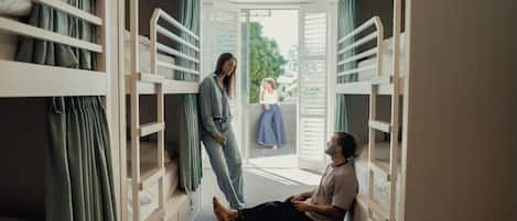 A room with bunk beds, a person sitting on the floor, and another person standing by the door.