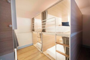 Una habitación pequeña con literas, piso de madera y un ventanal.