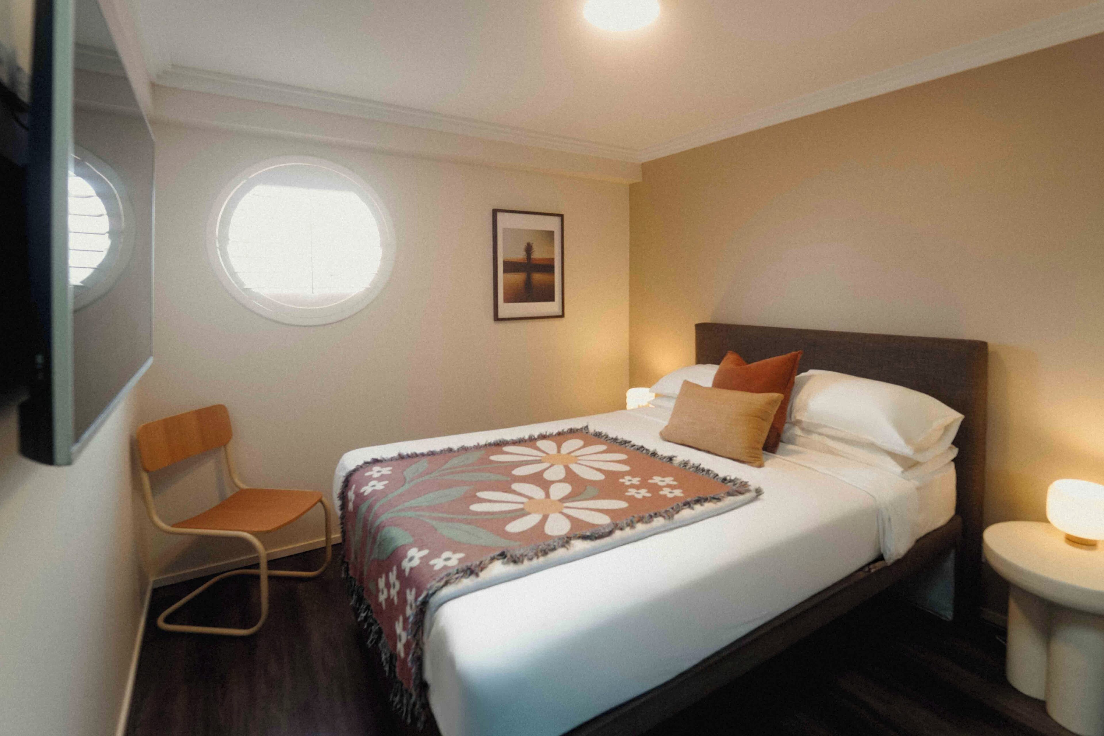 A hotel room with a bed, a chair, a small table, a window, and a picture on the wall.