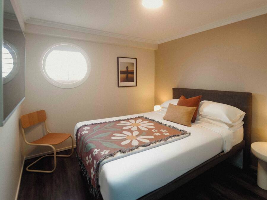 A hotel room with a bed, a chair, a small table, a window, and a picture on the wall.