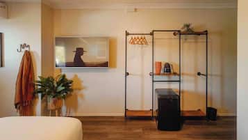 Una habitación con cama, perchero, planta en maceta, televisor, estantería metálica y maleta.