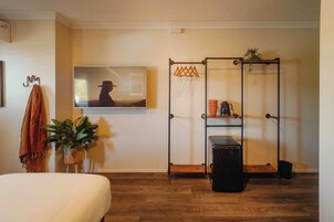 Una habitación con cama, perchero, planta en maceta, televisor, estantería metálica y maleta.