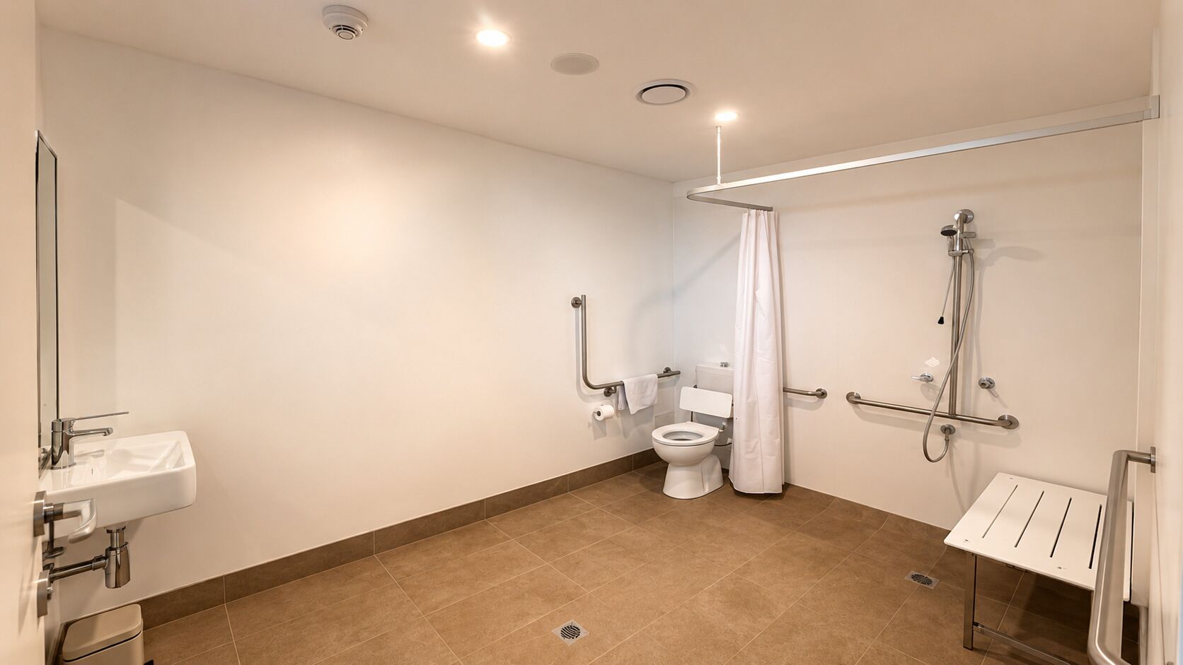 A modern bathroom with a toilet, sink, shower, and grab bars.