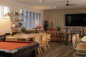 A modern living room with a pool table, a sofa, a TV, and a bar area.