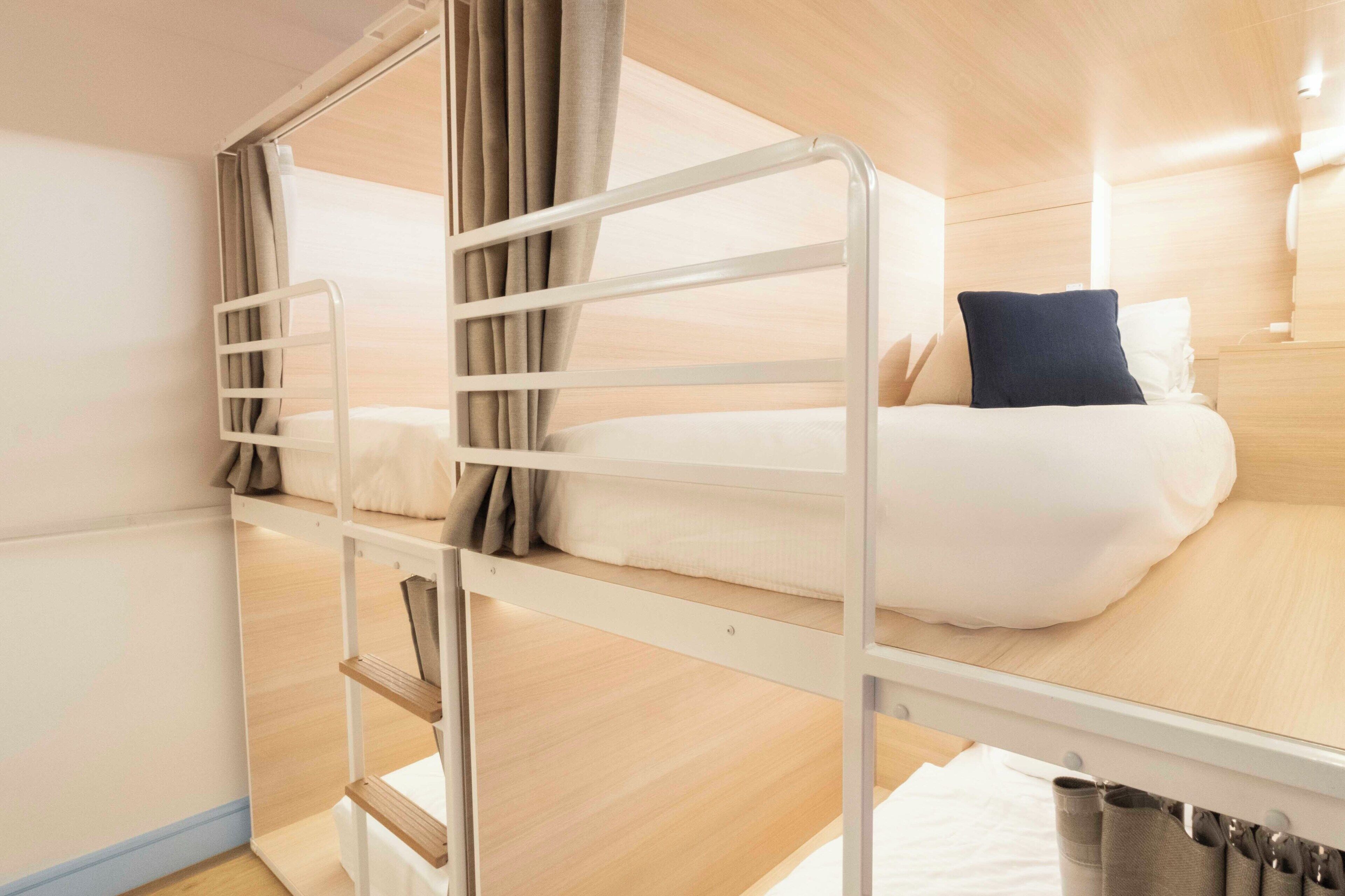 A bunk bed room with a wooden floor, white walls, and a curtain.