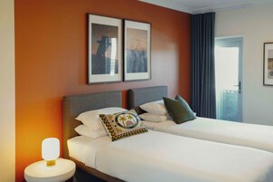 Una habitación de hotel con dos camas, una mesita de noche con lámpara y cuadros en la pared.