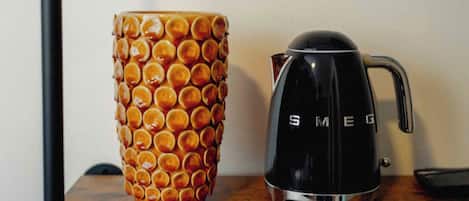 A black coffee maker with the brand name "SMEG" and a uniquely patterned orange mug on a wooden surface.
