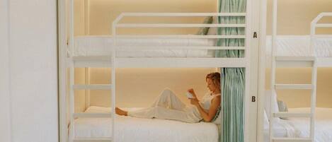 A bunk bed room with two beds, a person reading, and a green curtain.