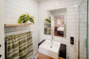Un baño con azulejos blancos, un lavabo, un espejo y dos plantas en macetas.