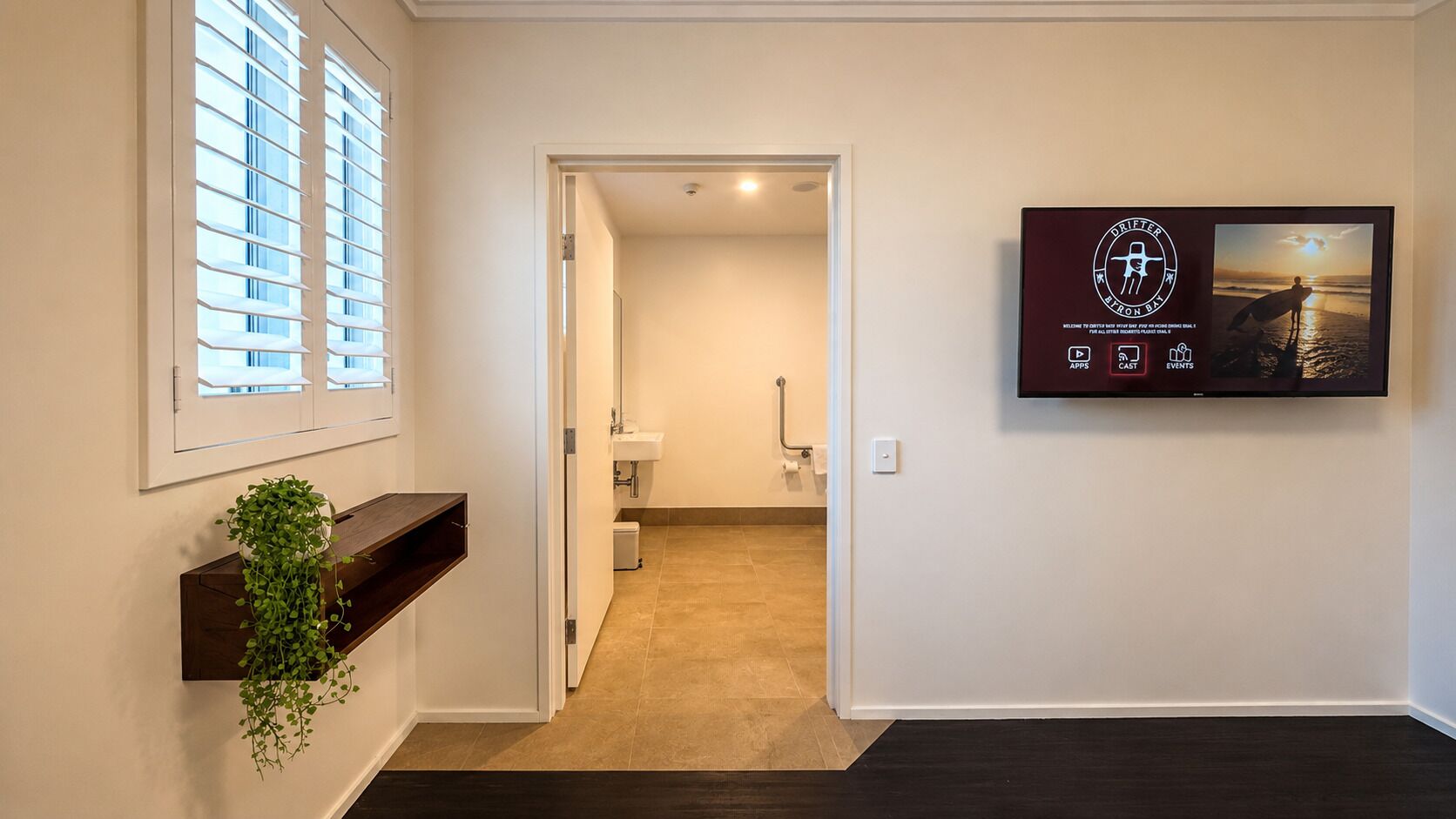A hallway with a plant shelf, a framed picture, and a door leading to a bathroom.