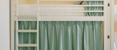 A bunk bed with a storage drawer below, a ladder, and a curtain.