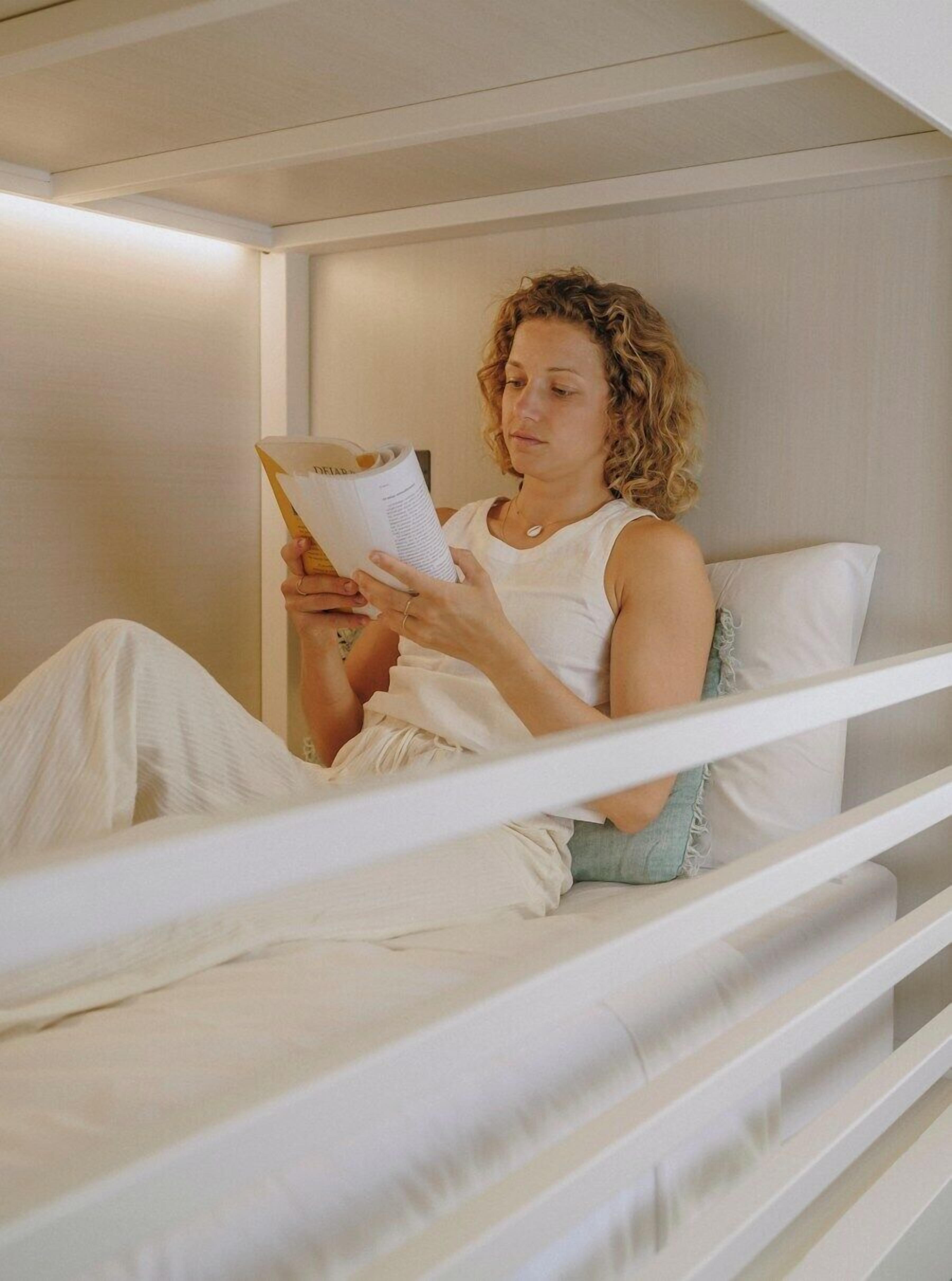 A person sitting in a bunk bed reading a book.