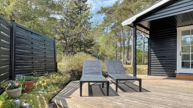 Une terrasse en bois avec deux chaises longues, une clôture noire et un bâtiment à l’extérieur sombre.