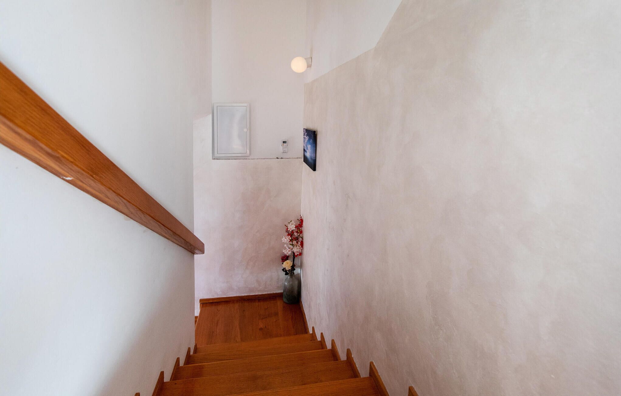 Een houten trap met een leuning, een wandlamp en een vaas met bloemen.