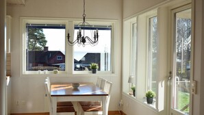 A dining area with a wooden table and chairs, a chandelier, and large windows with potted plants. - Amazing home in Rockneby with sauna (Rockneby)