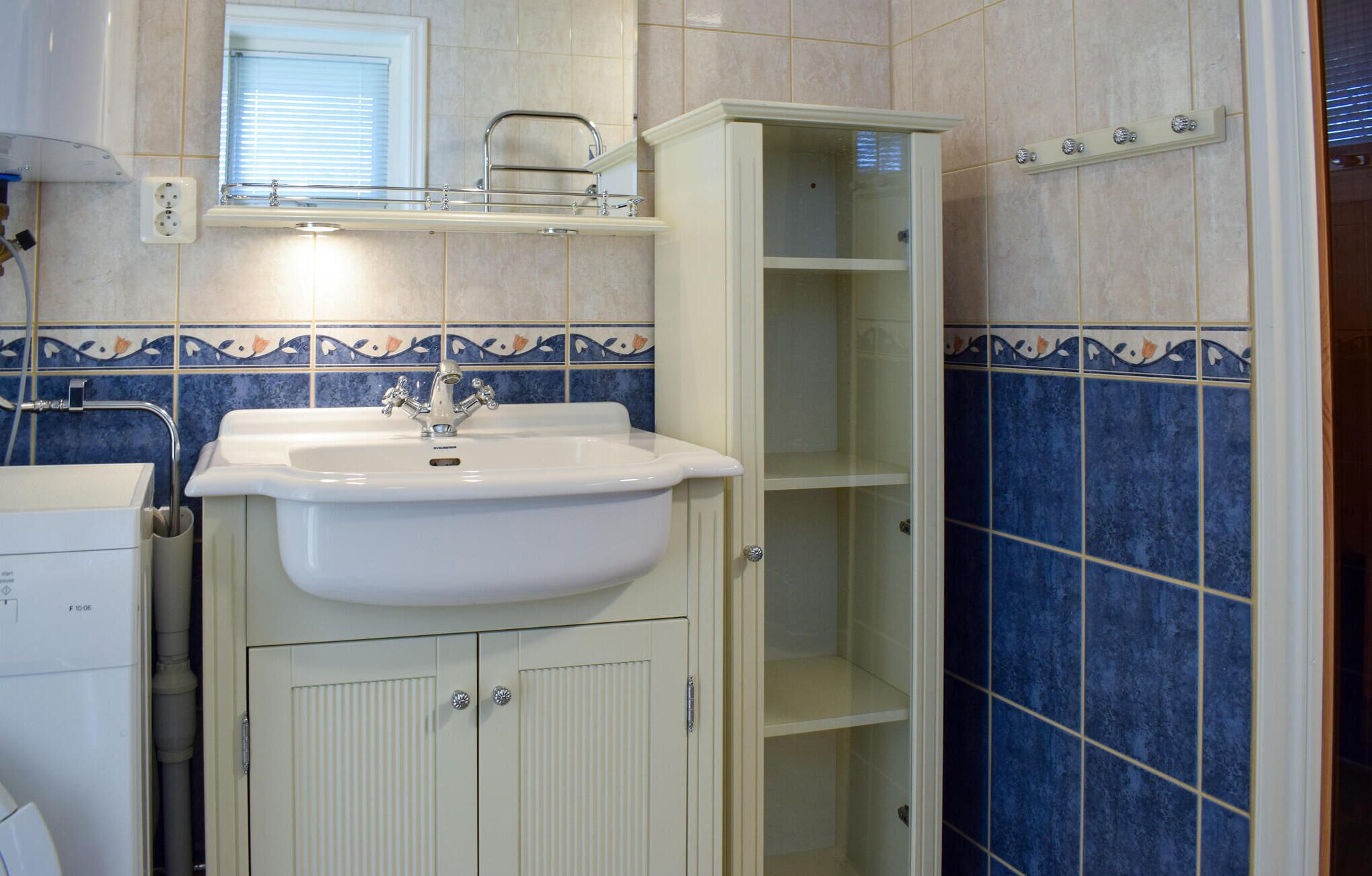 A bathroom with a white sink, a mirror above it, and a tiled wall with blue and beige tiles.