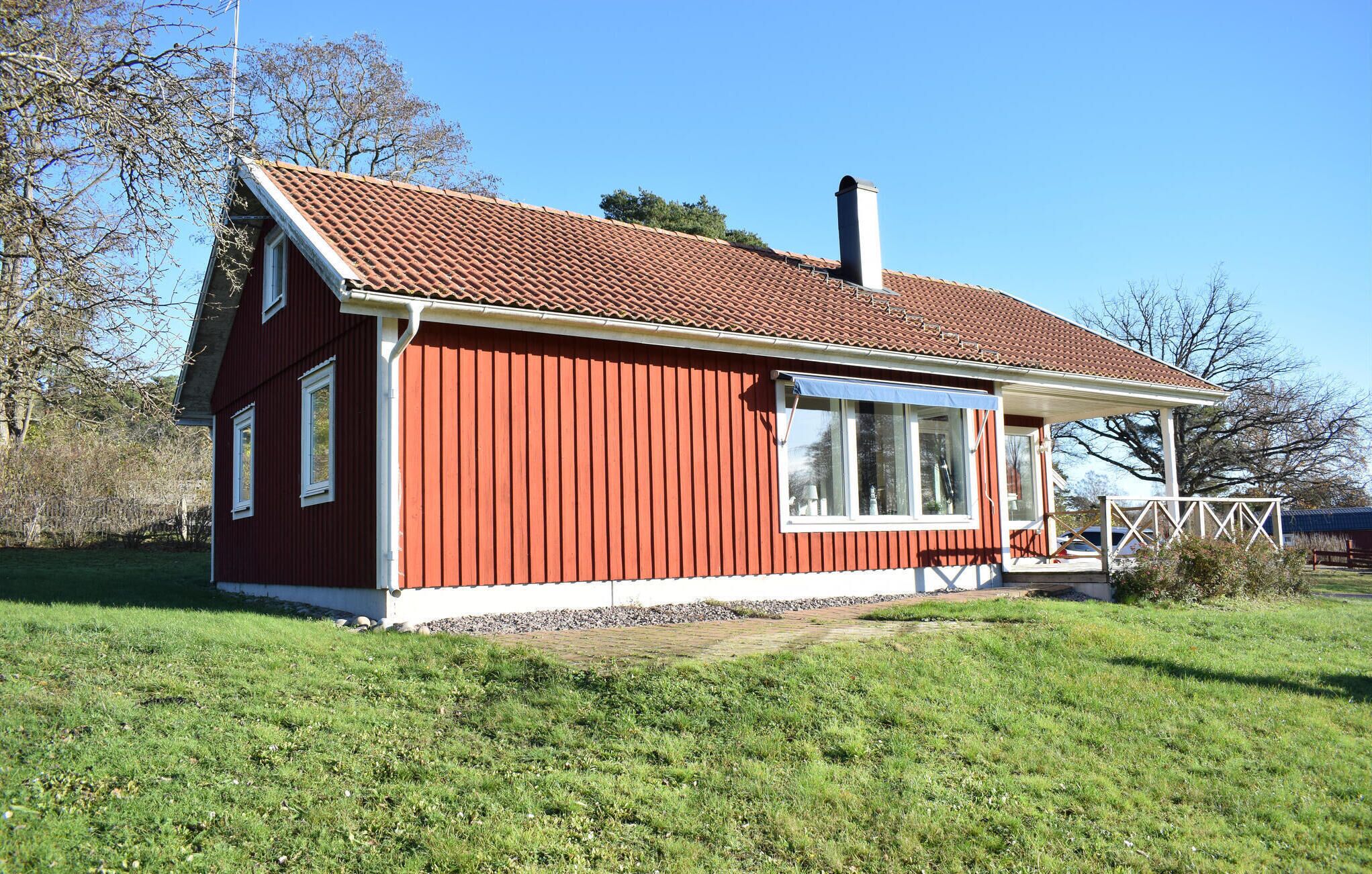 A red wooden house with a tiled roof, a chimney, and a porch with a white railing.