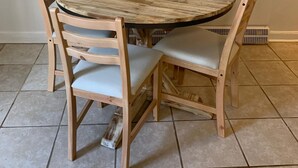 Een ronde houten eettafel met een schaal erop, omringd door vier houten stoelen met beklede zitplaatsen.