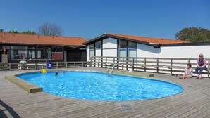 A swimming pool with a wooden deck, a building with a red-tiled roof, and a fence. - Amazing home in Allinge (Allinge)