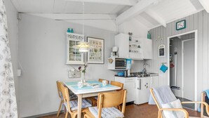 A compact kitchen with white cabinets, a microwave, and a coffee maker. There is a dining table with chairs and a hanging light fixture above it. - Amazing home in Allinge (Allinge)