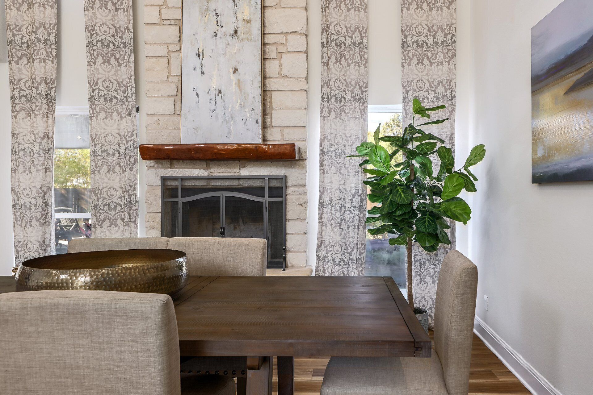 A dining area with a wooden table, cushioned chairs, a large decorative bowl, a fireplace, and a potted plant.