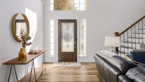 A spacious entryway with a wooden floor, a dark leather sofa, a wooden console table with a vase, a large mirror, and a decorative glass door. - North Austin Oasis near Domain  20 min to Downtown (Austin)