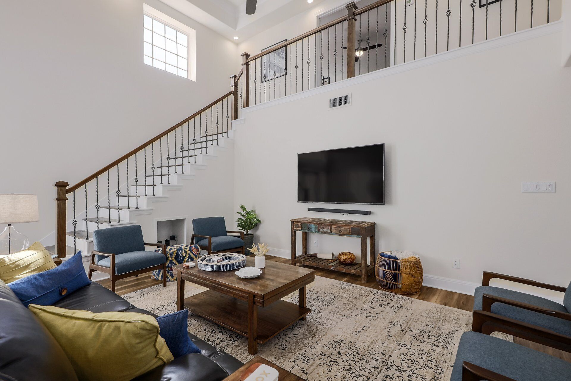 Ein geräumiges Wohnzimmer mit Treppe, einem an der Wand befestigten Flachbildfernseher und einem Couchtisch mit Dekoration.