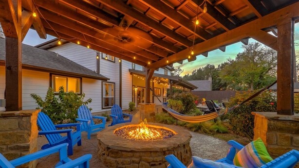 An outdoor patio with a stone fire pit, blue Adirondack chairs, and a hammock. - North Austin Oasis near Domain  20 min to Downtown (Austin)