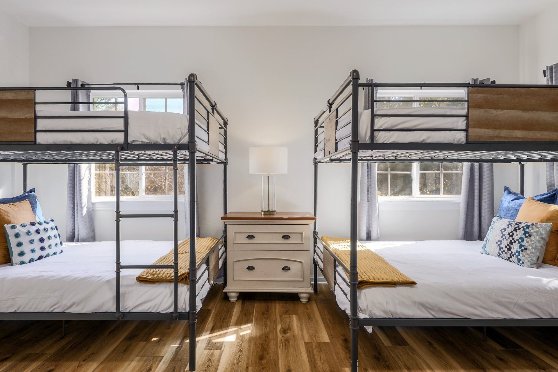 A room with two bunk beds, a bedside table with drawers, and a window with curtains.