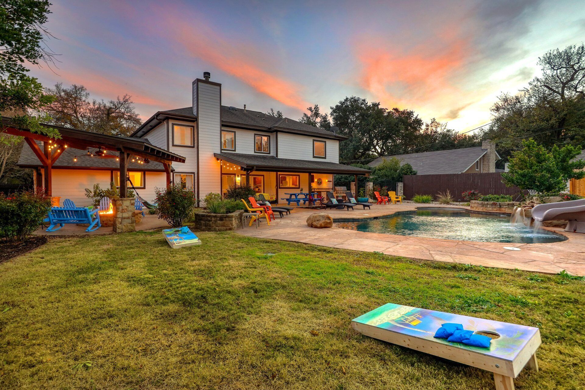 A two-story house with a backyard featuring a swimming pool, outdoor seating, and a covered patio area.